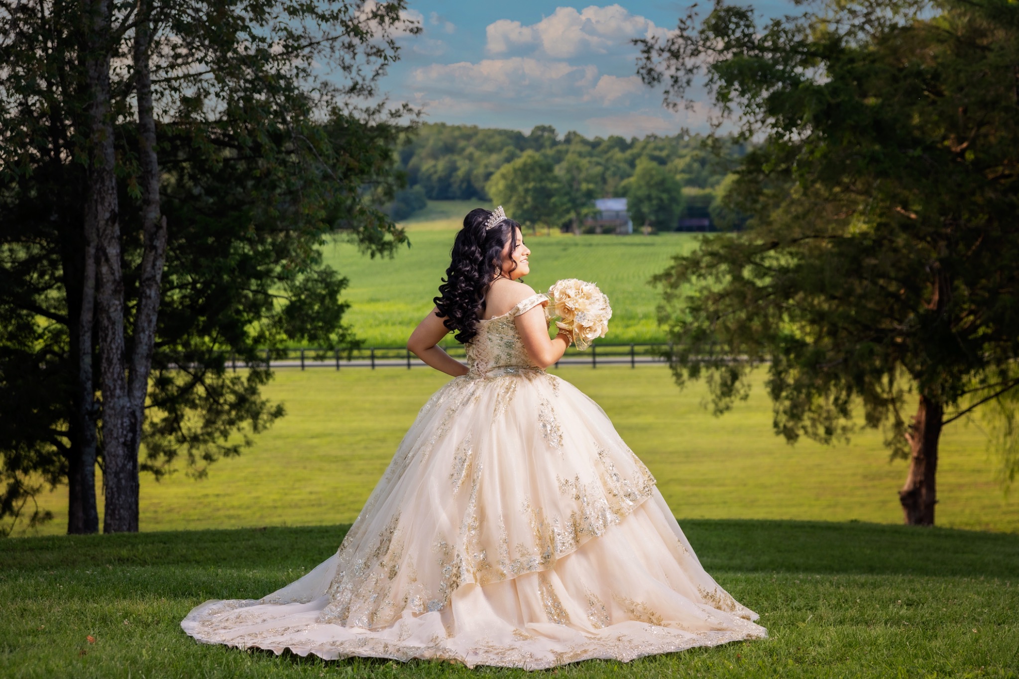 Quinceañera in an ivory gown overlooking a green landscape